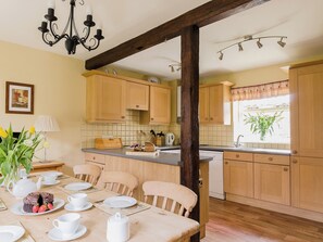 A kitchen with wooden cabinets, a dining table set with plates, cups, and a teapot, and a window with a plant. - 4 bedroom accommodation in Pickering (Pickering)