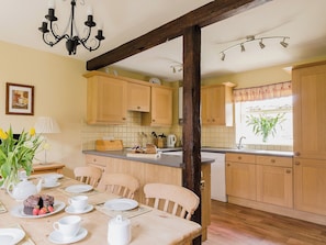 A kitchen with wooden cabinets, a dining table set with plates, cups, and a teapot, and a window with a plant.