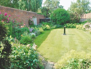Ein Garten mit Backsteinmauer, Rasenfläche und verschiedenen Pflanzen.