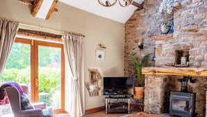 A cozy living room with a stone wall, a fireplace, a television, and a comfortable seating area. - An attractive and spacious cottage close to the River Eamont. (Pooley Bridge, nr. Ullswater)