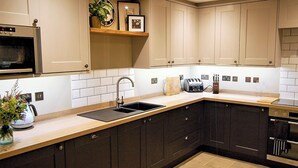 A modern kitchen with dark cabinets, a sink, a microwave, and a toaster. - An attractive and spacious cottage close to the River Eamont. (Pooley Bridge, nr. Ullswater)
