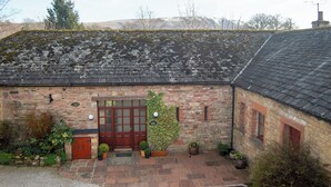 A stone building with a tiled roof, a wooden door, and potted plants. - An attractive and spacious cottage close to the River Eamont. (Pooley Bridge, nr. Ullswater)