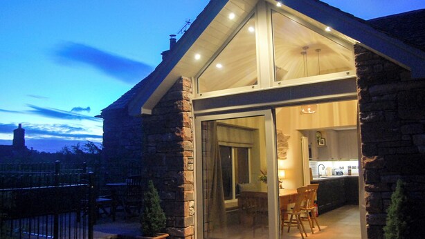 A modern house with a large glass door leading to a dining area. - An attractive and spacious cottage close to the River Eamont. (Pooley Bridge, nr. Ullswater)