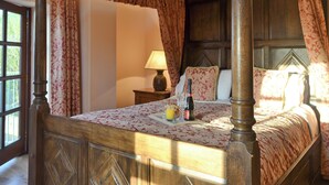 A four-poster bed with a floral bedspread, a bedside table with a lamp, and a bottle of champagne. - 2 bedroom accommodation in Glynarthen, near Cardigan (Glynarthen, near Cardigan)