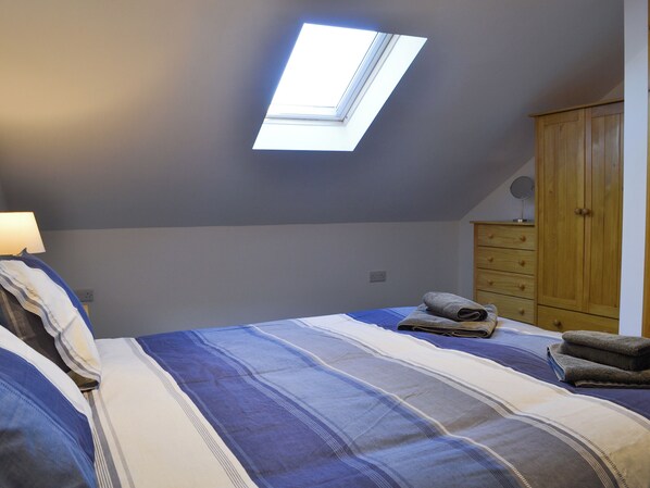 A bedroom with a skylight, a bed with striped bedding, a wooden wardrobe, and a bedside lamp.