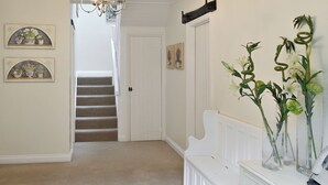 A hallway with a staircase, a chandelier, framed artwork, and a white console table with vases. - 4 bedroom accommodation in East Allington, near Totnes (East Allington, near Totnes)