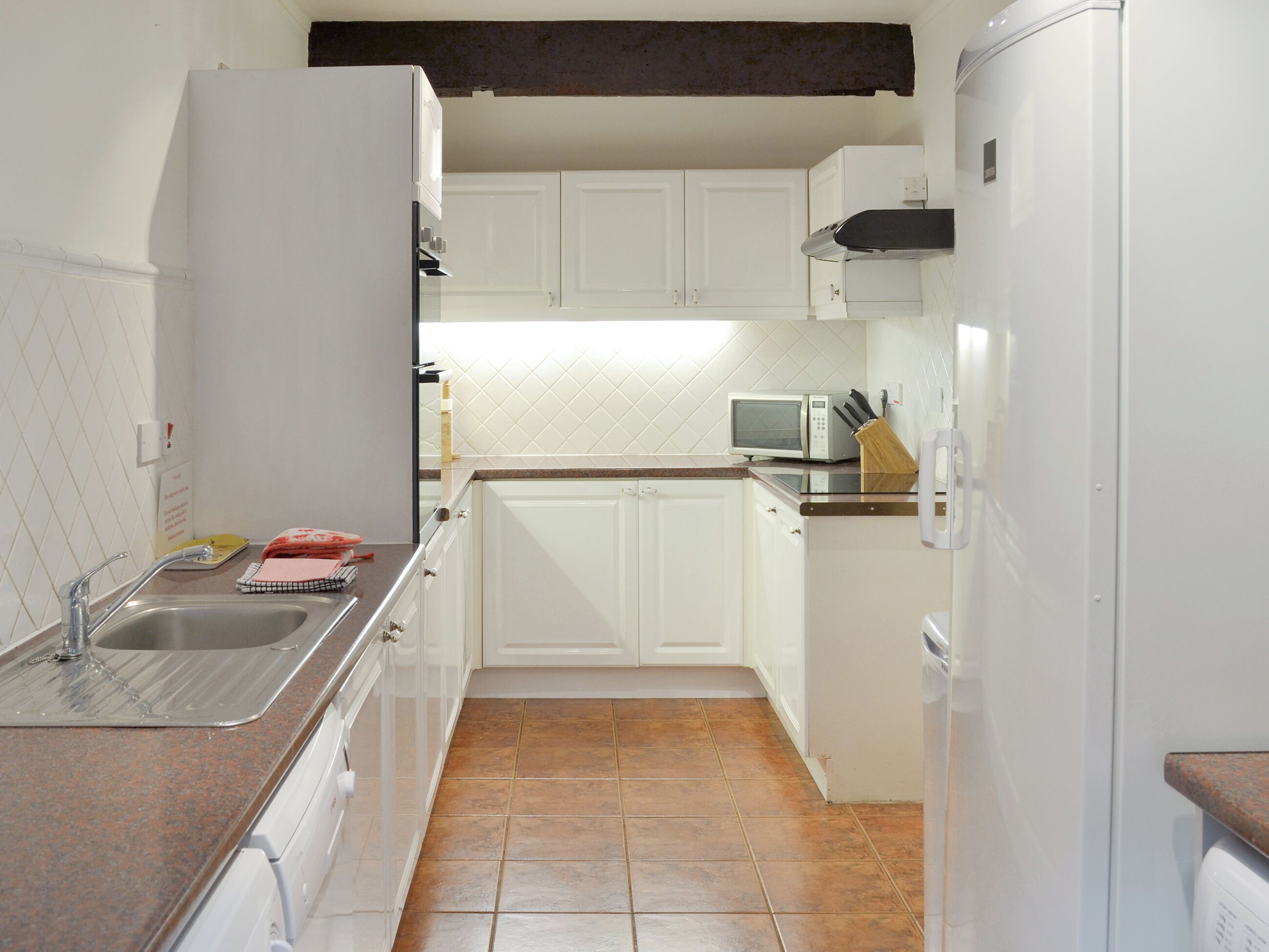A compact kitchen with white cabinets, a sink, a microwave, and a refrigerator.