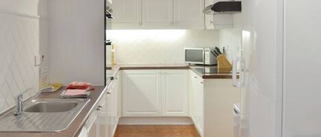 A compact kitchen with white cabinets, a sink, a microwave, and a refrigerator.