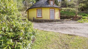 Una pequeña cabaña amarilla con cimientos de piedra, techo de paja y una ventana con marco de madera.
