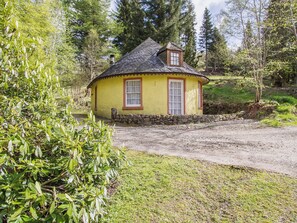 Une petite maison jaune aux murs de pierre, avec un toit de chaume et une fenêtre à cadre en bois.