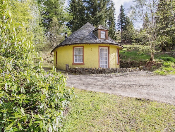 A small yellow cottage with a stone foundation, a thatched roof, and a window with a wooden frame.