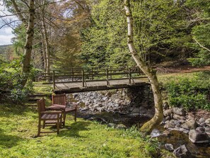 A wooden bridge over a stream, surrounded by trees and a bench.