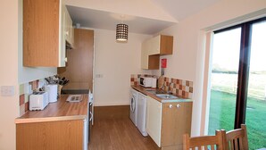 A compact kitchen with a washing machine, a sink, and a dining area with a table and chairs. - Russet Cottage - E4678 (Near Lympsham)
