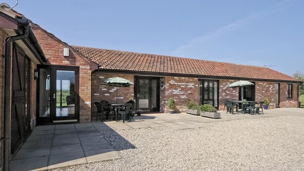 A building with a brick facade, a tiled roof, and outdoor seating with umbrellas. - Russet Cottage - E4678 (Near Lympsham)
