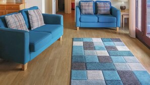A living room with two blue sofas, a wooden floor, and a checkered rug. - Russet Cottage - E4678 (Near Lympsham)