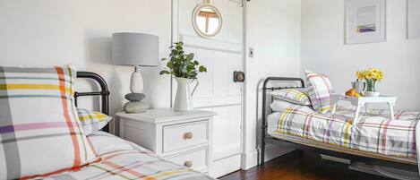 A bedroom with two beds, a bedside table with a lamp, a small table with flowers, and a door with a sign.