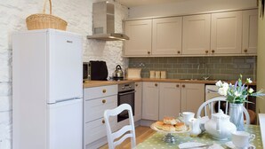 Eine kompakte Küche mit weißen Schränken, einem Beko-Kühlschrank, einer Mikrowelle und einem Wasserkocher auf der Arbeitsplatte.