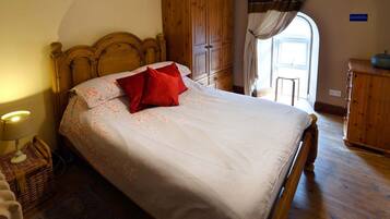 Een slaapkamer met een houten bed, nachtkastje, rieten stoel, houten kledingkast en een raam met gordijnen.