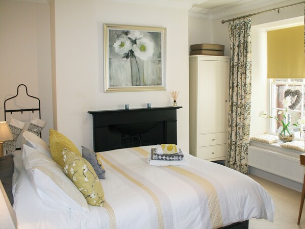 A neatly arranged bedroom with a bed, a dresser, a painting, and a window with curtains.