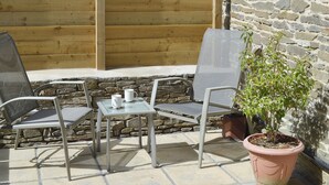 Une terrasse avec deux chaises et une table, une plante en pot et un mur en pierre.