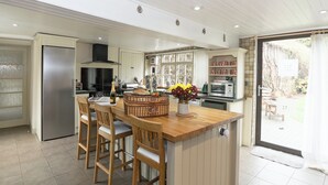 A modern kitchen with a central island, bar stools, a refrigerator, a microwave, and a dining area with a view of the outdoors. - Greenlands Farmhouse (Barmby Moor, York)