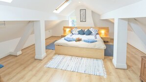 A modern bedroom with a sloped ceiling, a large bed with multiple pillows, bedside lamps, and a skylight. - Greenlands Farmhouse (Barmby Moor, York)