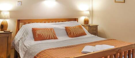 A neatly made bed with a wooden headboard, two bedside lamps, and a framed picture on the wall.