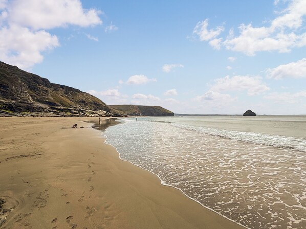 Une plage avec un ciel dégagé, une rive sablonneuse et des falaises rocheuses.