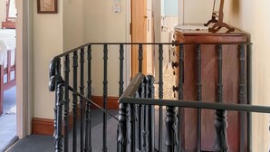 Un escalier orné de balustres noirs, une porte en bois et un miroir fixé à un meuble en bois.
