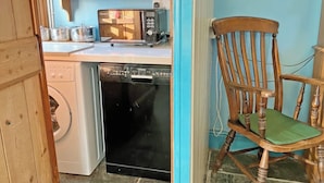 Une cuisine compacte équipée d’un lave-linge, d’un lave-vaisselle et d’un four à micro-ondes posé sur le plan de travail.