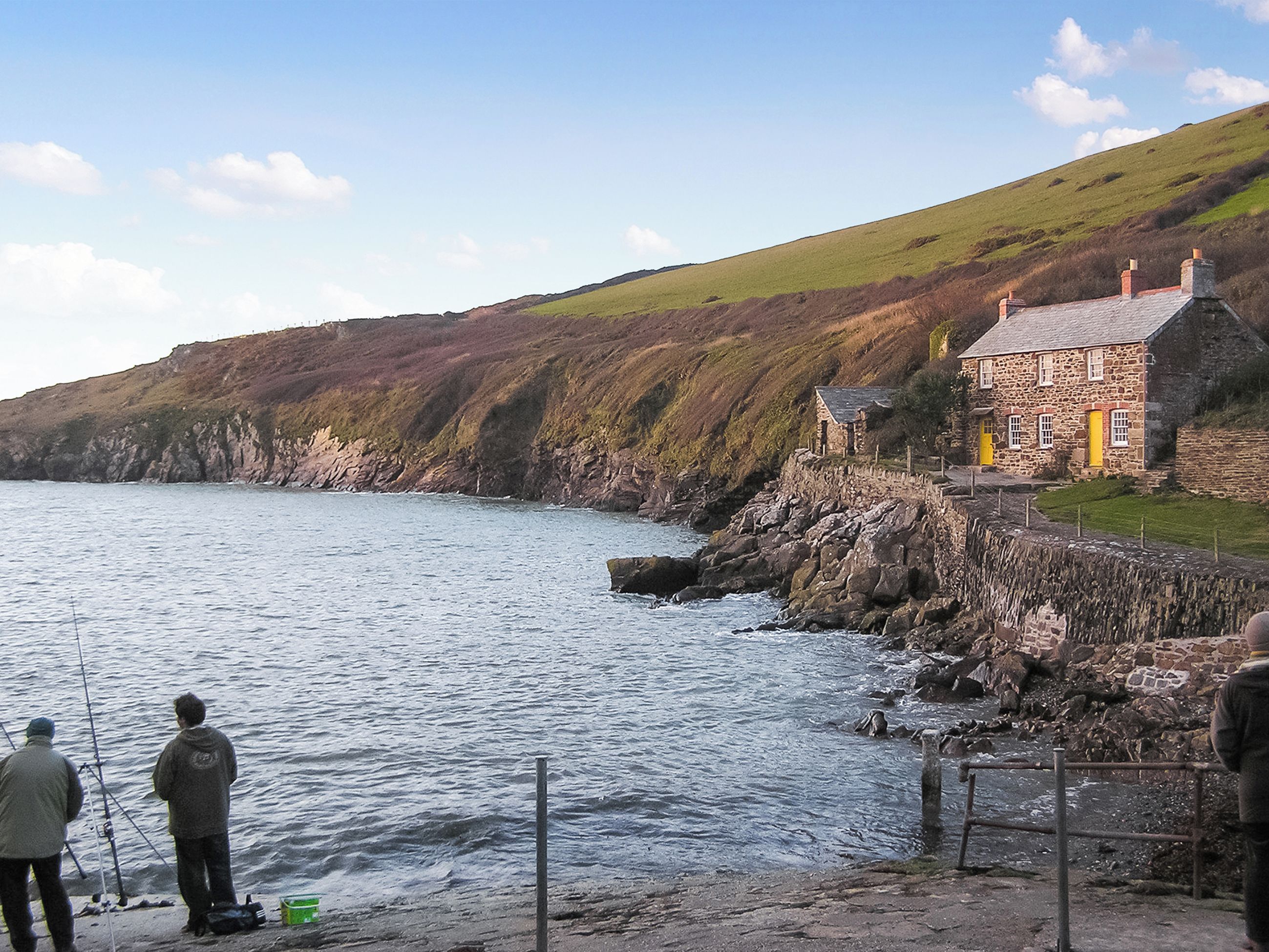 A coastal stone building with a stone staircase leading to a grassy area, overlooking a body of water.