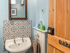 A bathroom with a white sink, a mirror, patterned tiles, a towel rack, and a wooden door.