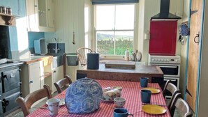 Une cuisine avec une nappe à carreaux rouges et blancs, un grand pichet en céramique bleue et une cuisinière.