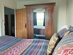 Une chambre avec une armoire en bois, un lit avec une literie à motifs et une fenêtre avec des rideaux.