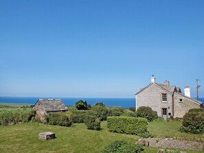 Une maison en pierre avec une cour verdoyante et une vue sur la mer.