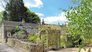 Une maison en pierre avec un jardin, une allée en gravier et une clôture en bois.