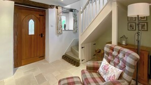 Un salon avec un fauteuil à motifs écossais, une porte en bois ornée d’un vitrail, un escalier et une lampe.