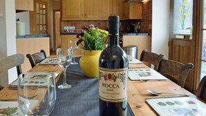 Une table à manger avec une bouteille de vin, des verres et un vase de fleurs.