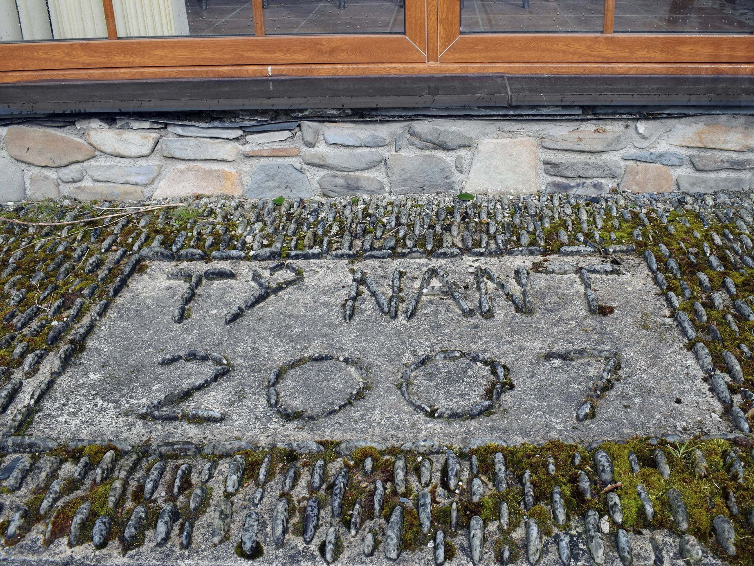 A stone plaque with the inscription "T7 NWT 2007" surrounded by moss and small stones.
