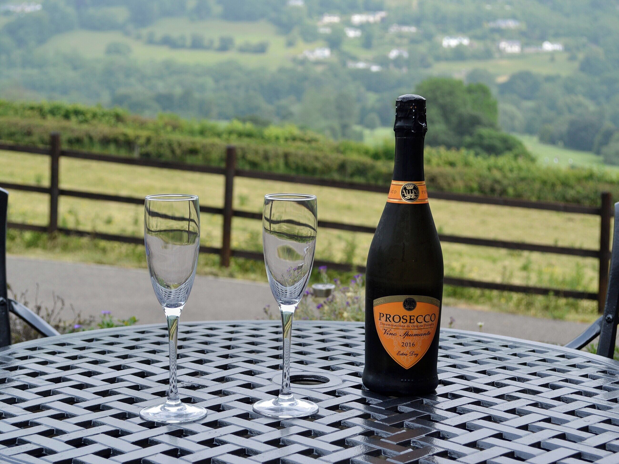 Eine Prosecco-Flasche und zwei Gläser auf einem Metalltisch, im Hintergrund eine schöne Aussicht.