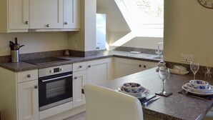 A kitchen with white cabinets, a built-in oven, a granite countertop, and a dining area with a table set for two. - 1 bedroom accommodation in Baslow, near Bakewell (Baslow, near Bakewell)