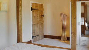 A bedroom with a wooden door, a bed with white bedding, a tall bedside table, and a wardrobe with a mirror. - 1 bedroom accommodation in Baslow, near Bakewell (Baslow, near Bakewell)