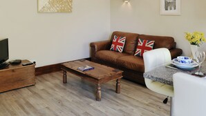 A living room with a brown leather sofa, a wooden coffee table, a white armchair, a small table with a vase of yellow flowers, and a framed picture on the wall. - 1 bedroom accommodation in Baslow, near Bakewell (Baslow, near Bakewell)