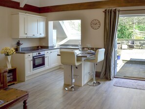 A modern kitchen with white cabinets, a built-in oven, and a dining area with two bar stools. - 1 bedroom accommodation in Baslow, near Bakewell (Baslow, near Bakewell)