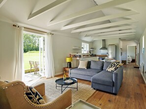 Ein geräumiges Wohnzimmer mit einem grauen Sofa, einem Holztisch und einem Essbereich im Hintergrund.