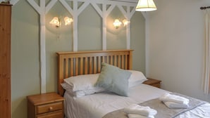 Una cama bien tendida con sábanas blancas, cabecera de madera y mesita de noche con cajones.