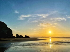 A beach with a sunset, clear sky, and rocky formations. - This 250-year-old farmhouse is ideal for a family seaside holiday. (Crantock, near Newquay)