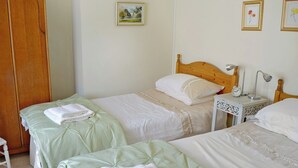 A bedroom with two beds, a wooden wardrobe, a bedside table with a lamp, and a small clock. - Pant Glas Mawr Axton (Axton, near Holywell)