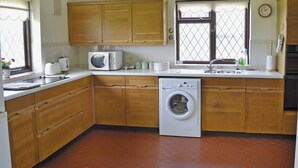 A compact kitchen with wooden cabinets, a microwave, a washing machine, and a sink. - Pant Glas Mawr Axton (Axton, near Holywell)