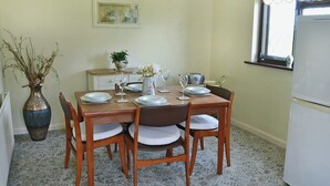 A dining room with a wooden table set for four, surrounded by chairs. There is a vase with flowers on the table, and a painting on the wall above it. - Pant Glas Mawr Axton (Axton, near Holywell)